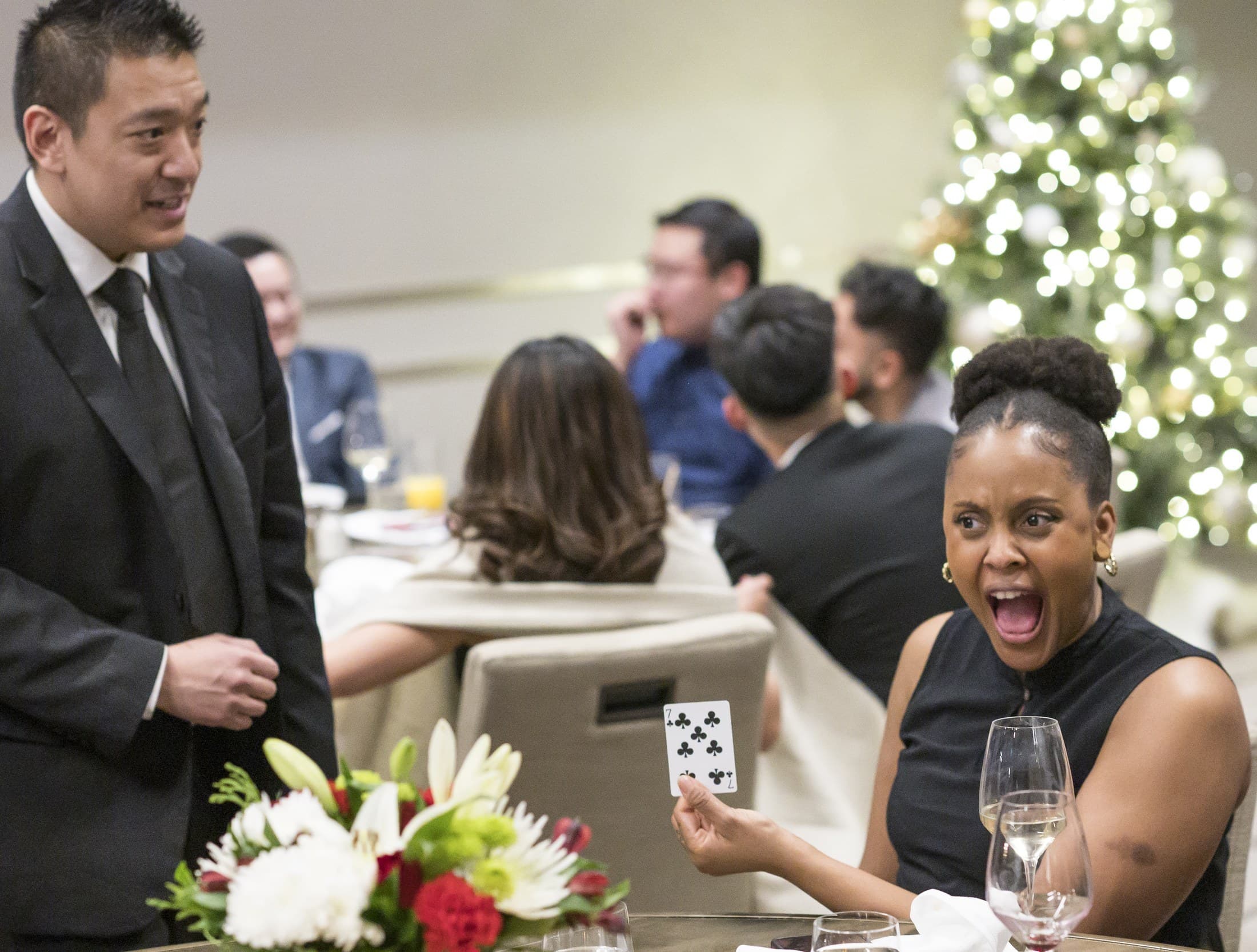 John Ha performing close-up magic for guests at a company Christmas party with a surprised reaction