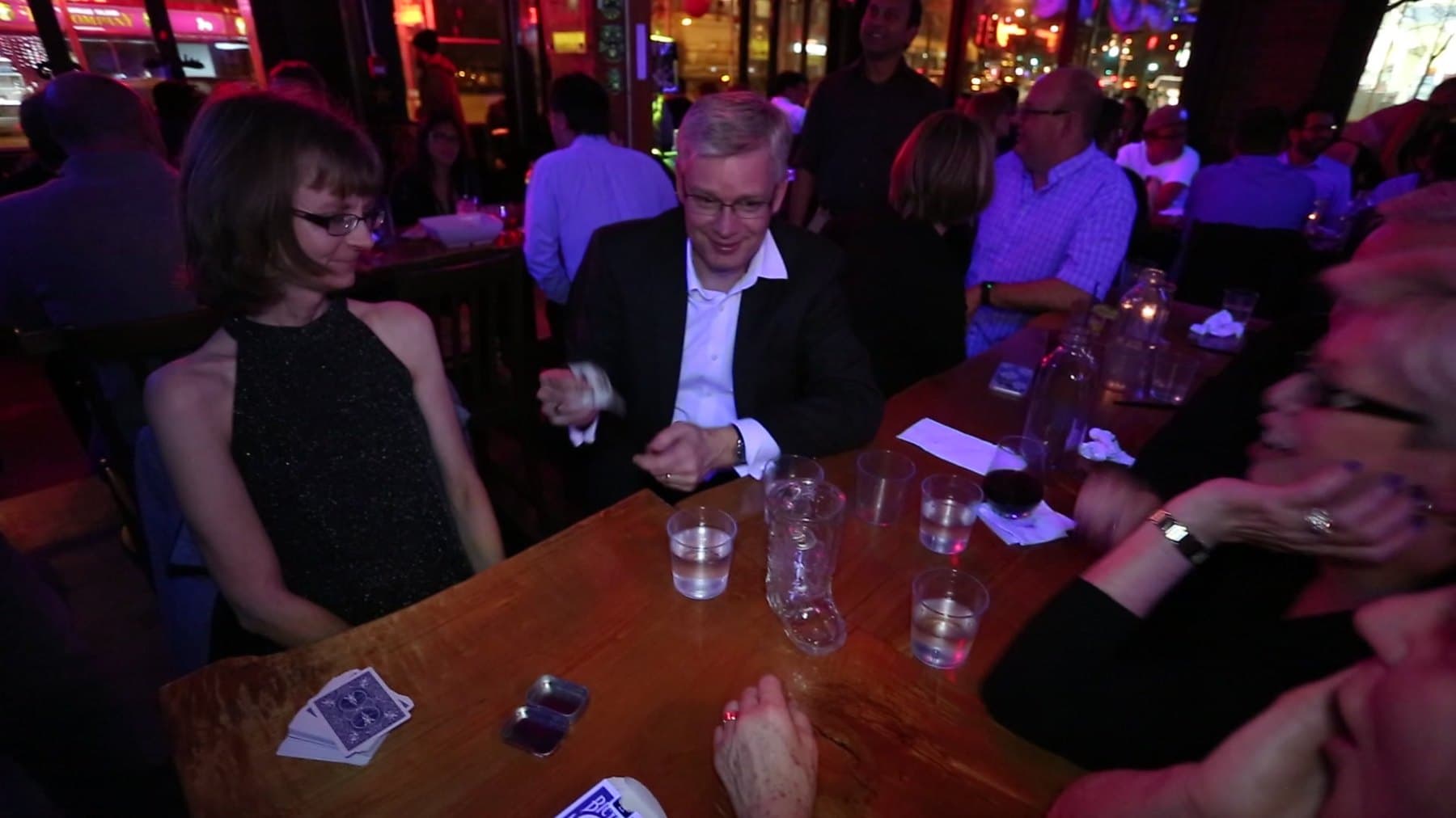 John Ha performing close-up card magic at a table while reception guests react and laugh